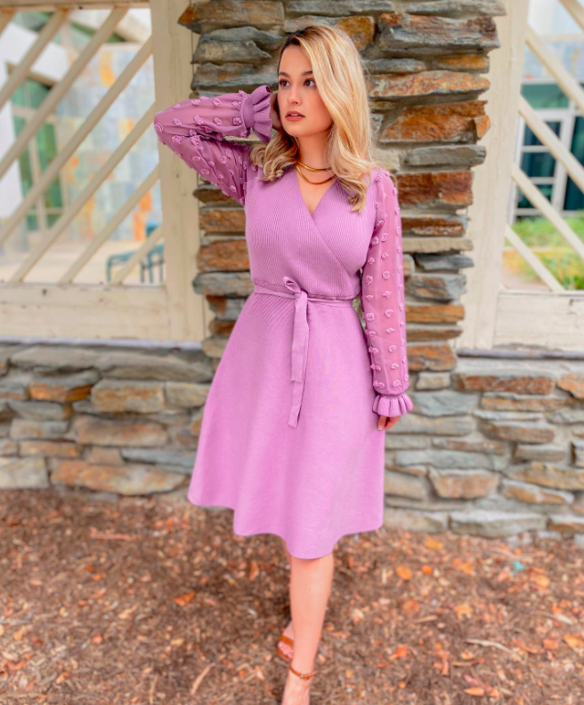 blogger wearing a lavender sweater wrap dress with bell sleeves, ruffled wrists, and lavender polka dots on the sleeves. The dress stops just below the knee and is one of the top-seliing dresses from the brand.