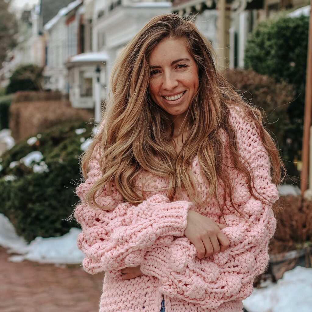 blogger wearing the pink bell sleeve chunky knit sweater with pom pom balls on the sleeves