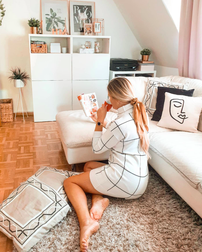 chicwish blogger wearing the white and black grid print dress while sitting on the floor reading a book as they lean against the couch