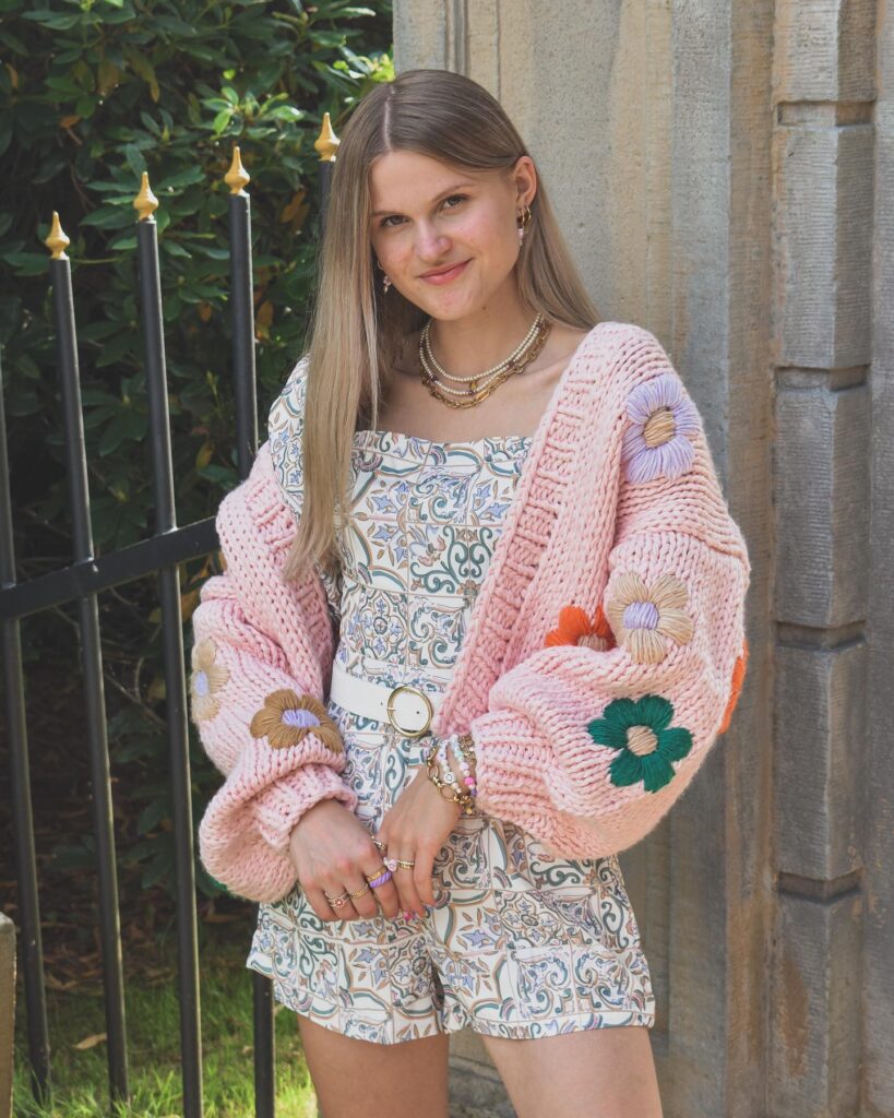 blogger wearing a pink chunky cable knit sweater with colorful flowers embroidered onto it