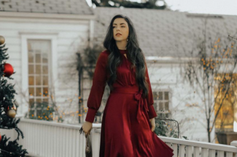 blogger wearing a red wrap holiday dress and standing in front of a house beside a decoarated christmas tree