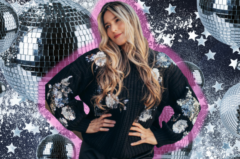 woman wearing a black sweater with sequin embellishments standing in front of a disco ball background