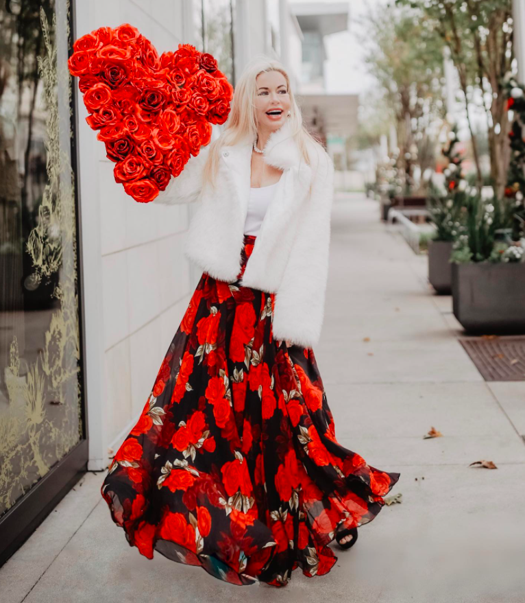 blogger wearing a red rose printed maxi skirt with a faux fur whtie jacket and white top and a bouquet of heart-shaped flowers for a Valentine's Day shoo
